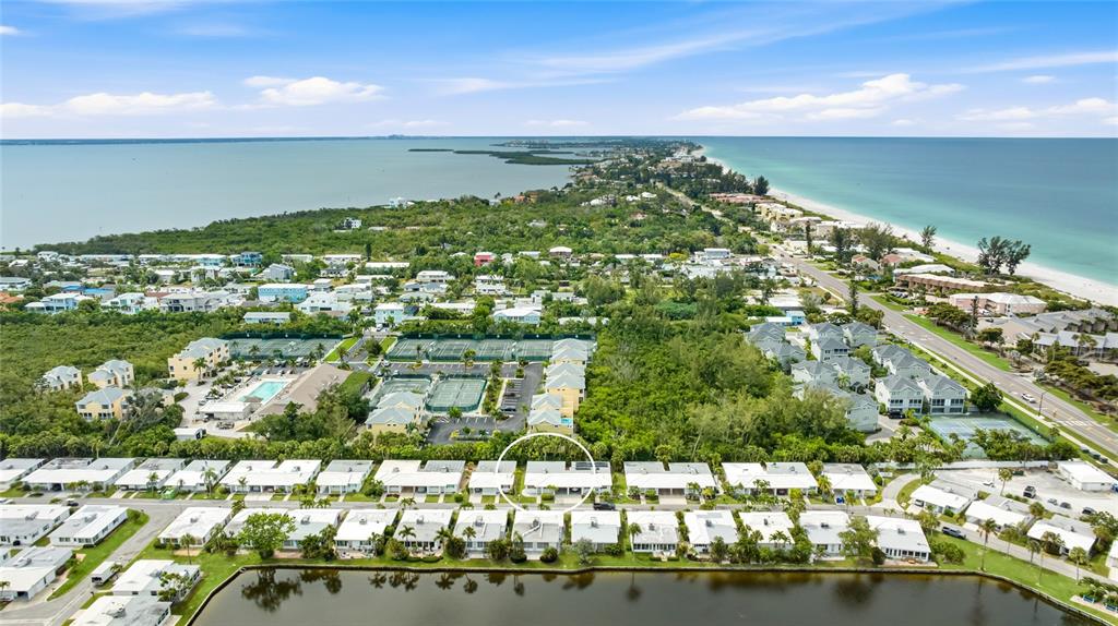 An aerial view shows a residential complex with white-roofed townhomes bordering a small lake — 602 SPANISH DRIVE S UNIT 115, LONGBOAT KEY, FL