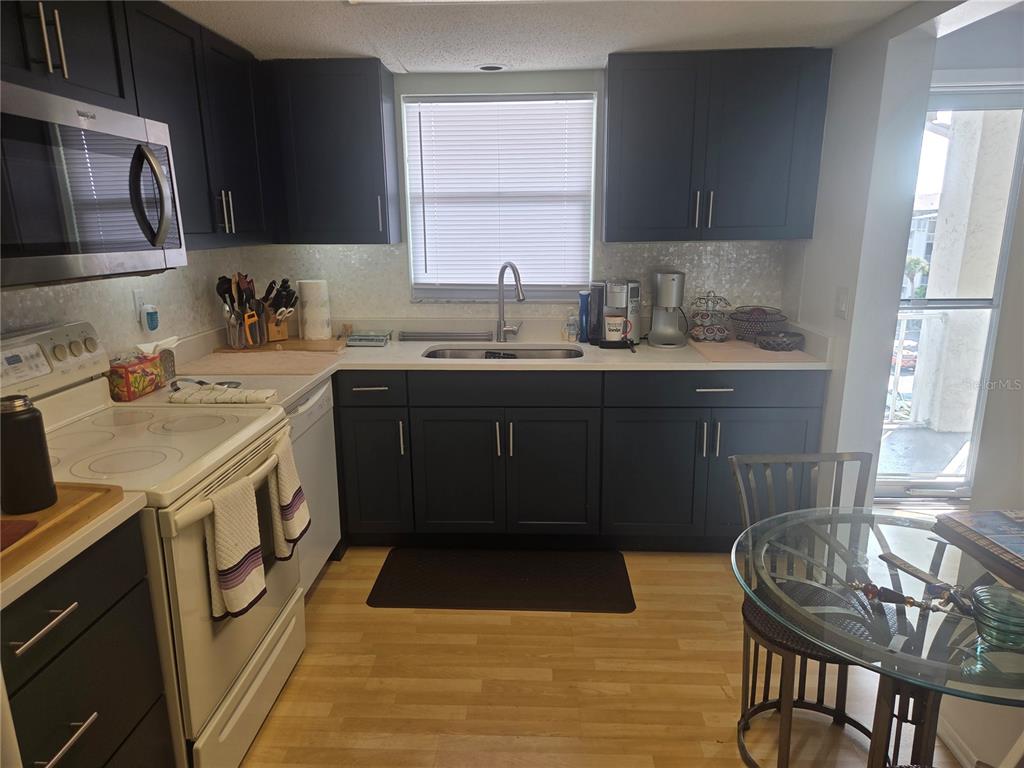 A kitchen features dark cabinets, white countertops, a stainless steel sink, and a glass table — 3288 LAKE BAYSHORE DRIVE UNIT 523, BRADENTON, FL