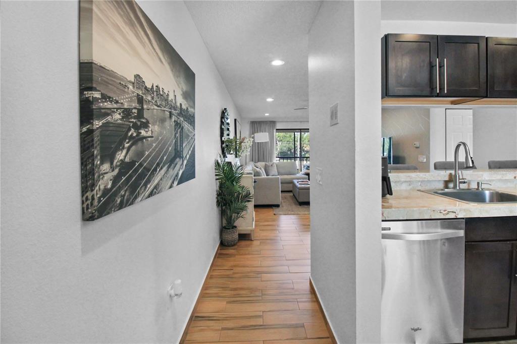 A hallway with wood-look tile floors leads from a kitchen toward a living room — 3001 58TH AVENUE S UNIT 408, ST PETERSBURG, FL