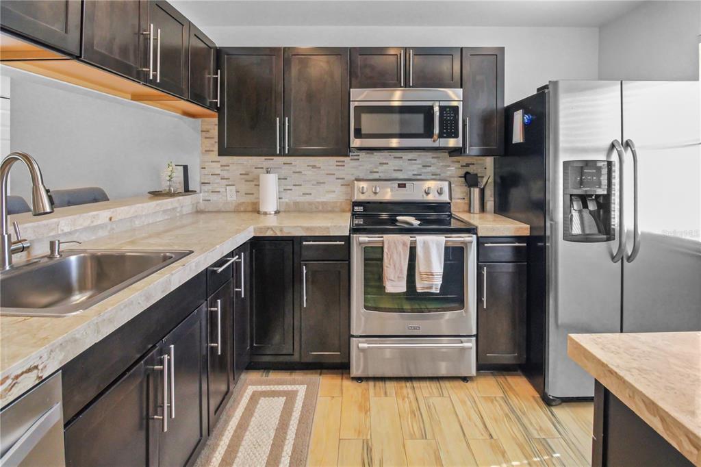 A kitchen features dark wood cabinets, stainless steel appliances, and light-colored stone countertops — 3001 58TH AVENUE S UNIT 408, ST PETERSBURG, FL