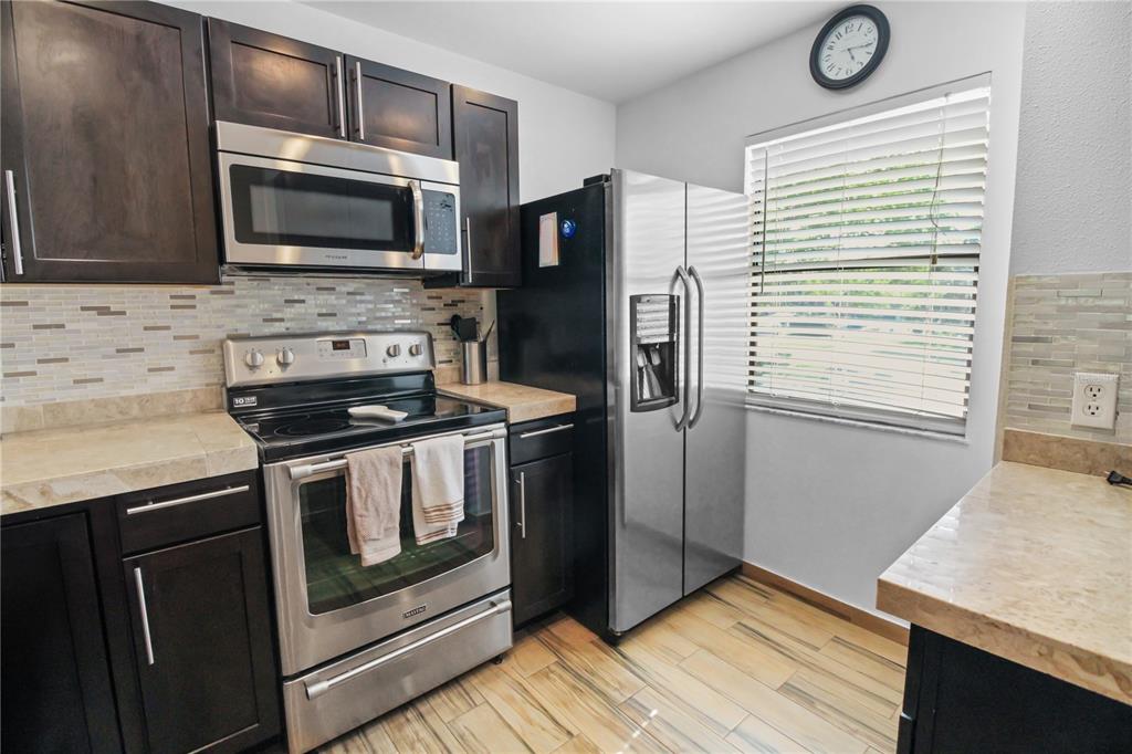 A kitchen features dark wood cabinets, stainless steel appliances, a tiled backsplash, and wood-look flooring — 3001 58TH AVENUE S UNIT 408, ST PETERSBURG, FL