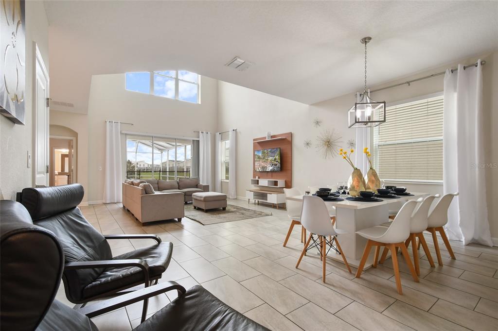 A bright, open-concept living and dining area features vaulted ceilings, tile floors, and large windows — 8942 CABOT CLIFFS DRIVE, DAVENPORT, FL
