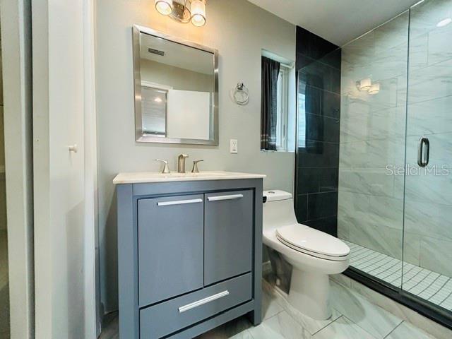 A bathroom features a gray vanity, a toilet, and a glass-enclosed shower with tiled walls — 1914 CHAMBERLIN STREET, ORLANDO, FL