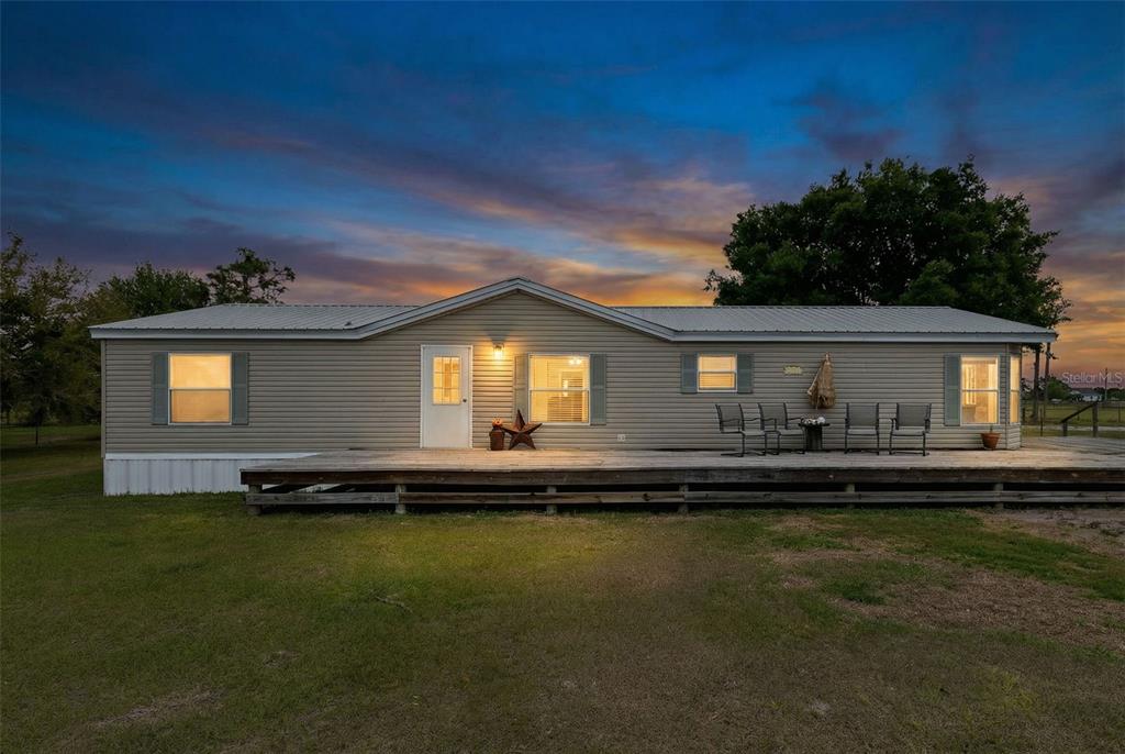 A single-story manufactured home with light siding and a large wooden deck at sunset — 3591 N CANOE CREEK ROAD, KENANSVILLE, FL