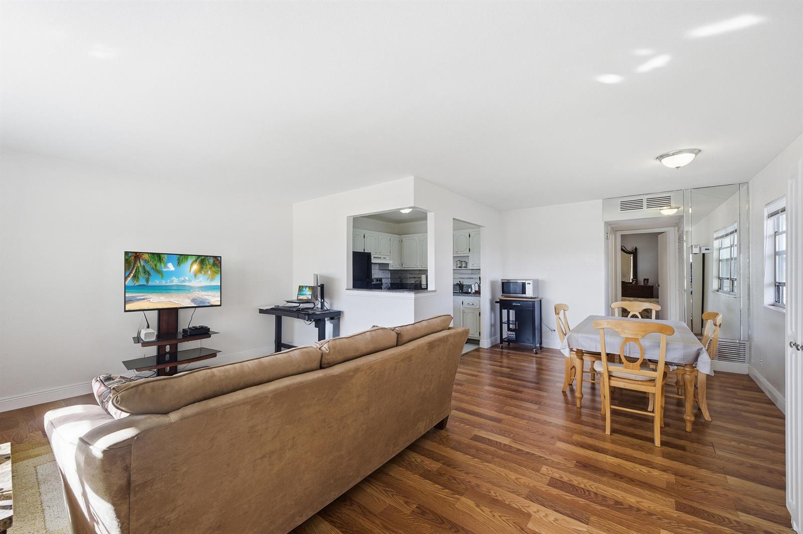 A living and dining area with wood-look flooring, white walls, and an open kitchen pass-through — 142 Monaco C, Delray Beach FL 33446, DELRAY BEACH, FL
