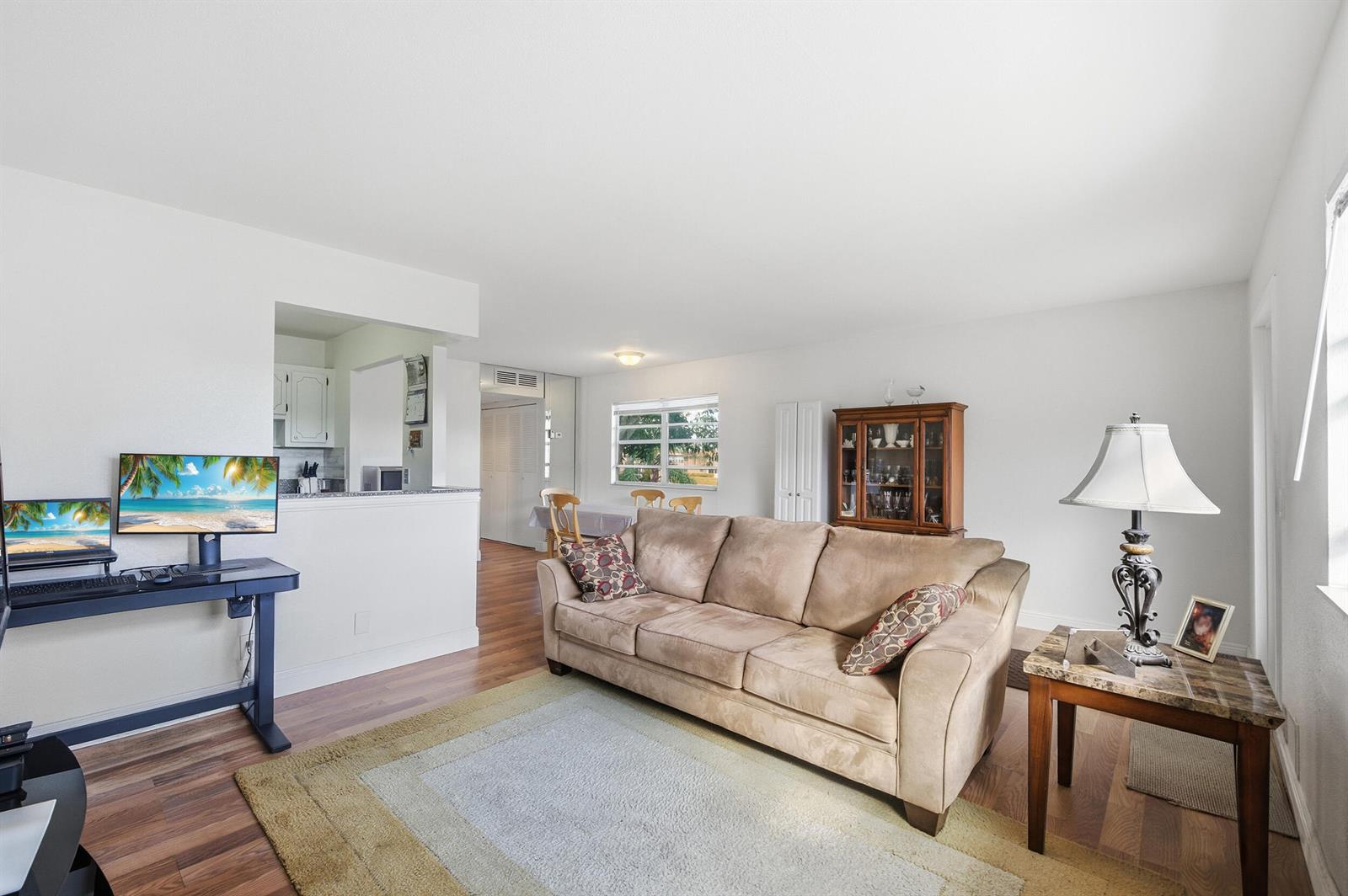 A living room features a beige sofa, a desk with a computer, and wood-look flooring — 142 Monaco C, Delray Beach FL 33446, DELRAY BEACH, FL