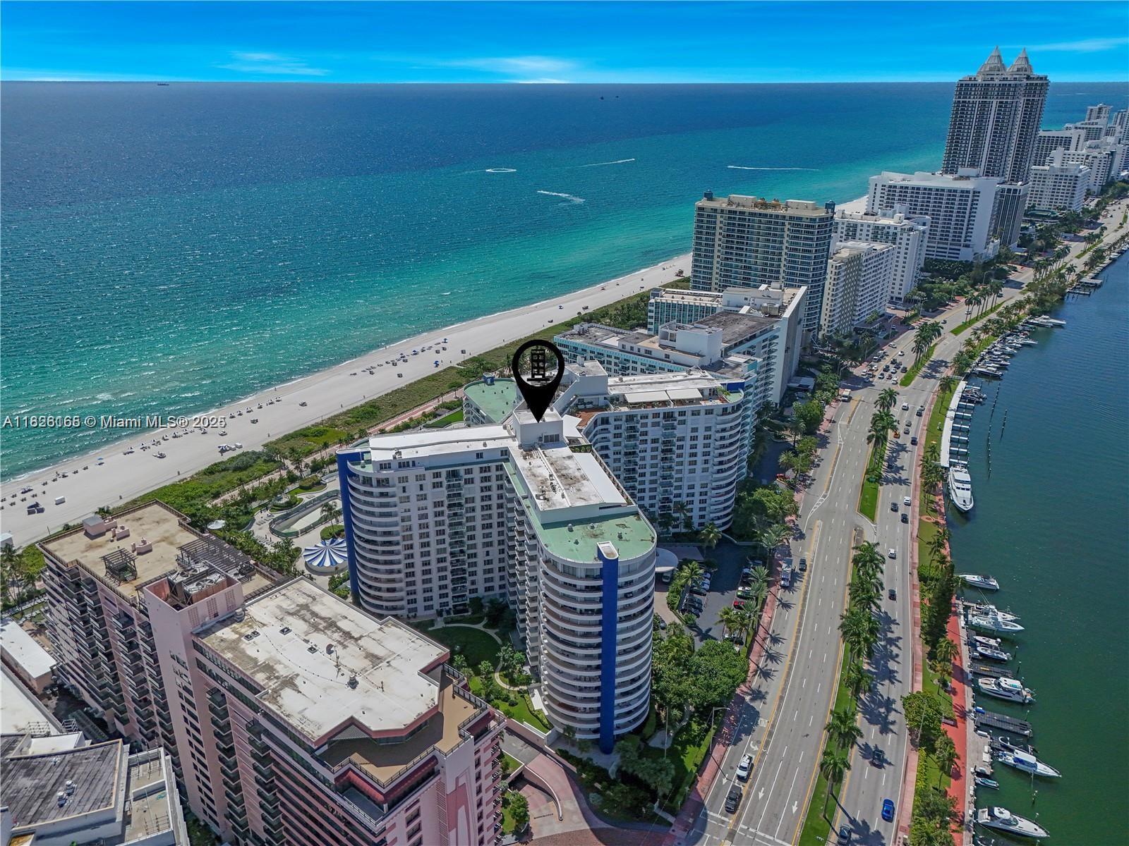 An aerial view shows a multi-story residential building located between the ocean and a canal — 5151 Collins Ave # 535, Miami Beach FL 33140, MIAMI BEACH, FL