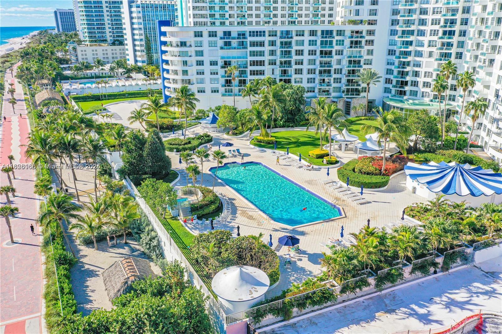 An aerial view of a large swimming pool surrounded by palm trees and apartment buildings — 5151 Collins Ave # 535, Miami Beach FL 33140, MIAMI BEACH, FL