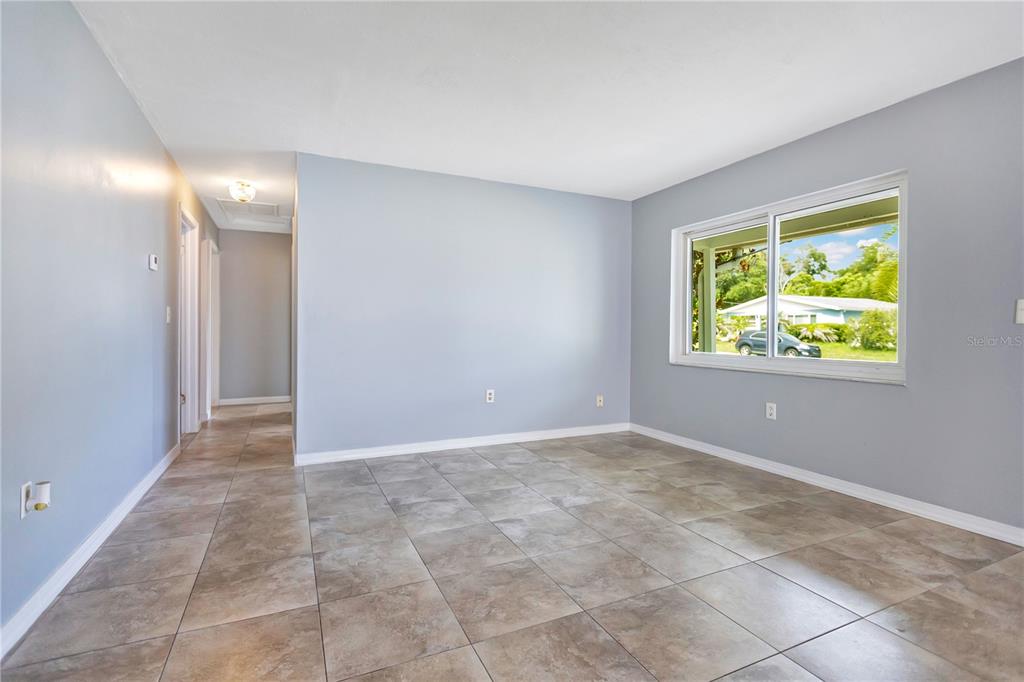 A room with light gray walls and tiled flooring transitions into a kitchen with cabinets — 8316 TUPELO DR, TEMPLE TERRACE, FL