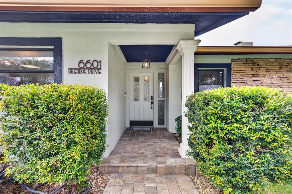 The front entrance features a white door, stone walkway, and large green bushes — 6601 BRENDA DRIVE, APOPKA, FL