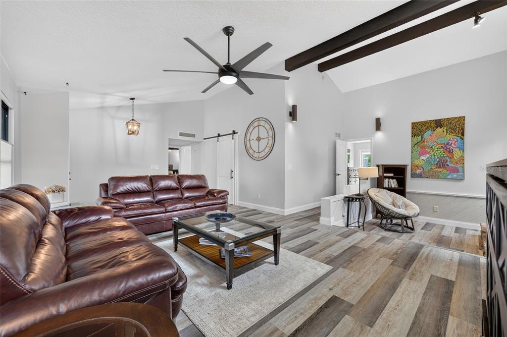 A living room features leather sofas, a glass coffee table, wood-look flooring, and vaulted ceilings — 6601 BRENDA DRIVE, APOPKA, FL