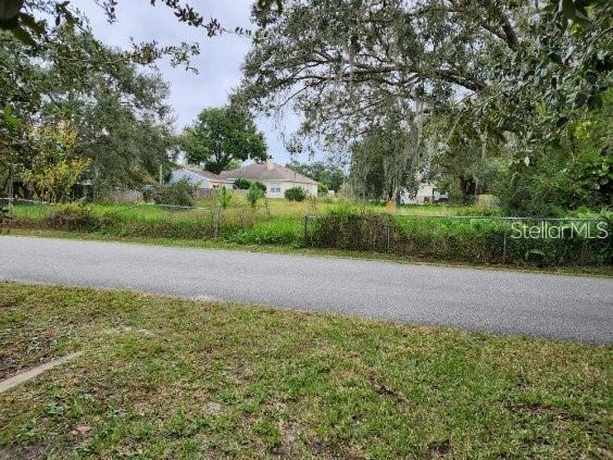 A vacant, grassy lot sits behind a chain-link fence along a paved residential street — 4947 PETROFF AVENUE, ORLANDO, FL