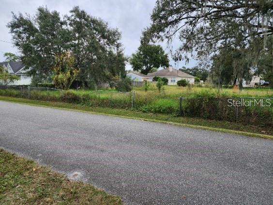 A vacant, grassy residential lot is enclosed by a chain-link fence along a paved road — 4947 PETROFF AVENUE, ORLANDO, FL