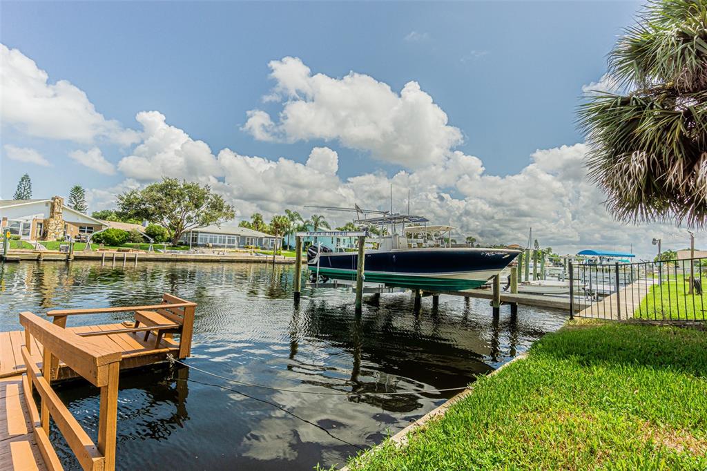A boat is docked on a lift in a canal next to a wooden pier — 4149 FLORAMAR TERRACE, NEW PORT RICHEY, FL