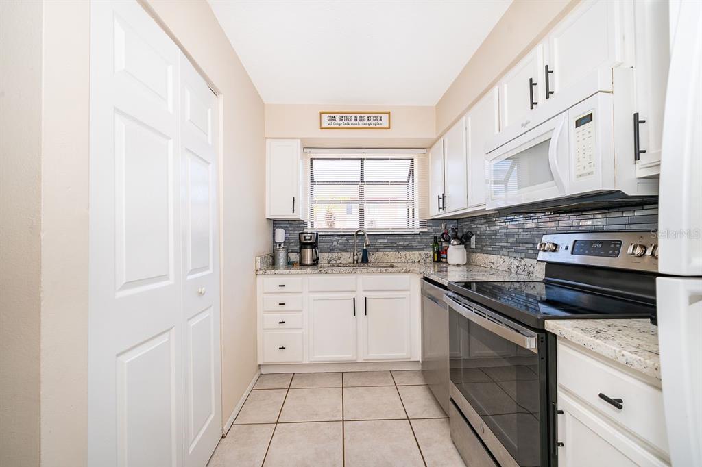 A galley kitchen features white cabinets, granite countertops, stainless steel appliances, and a tiled backsplash — 129 WHITE FAWN DRIVE UNIT 1290, DAYTONA BEACH, FL