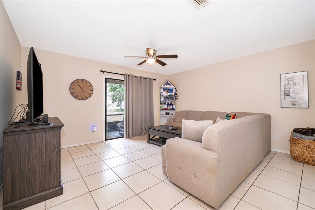 A living room features beige tile flooring, a sectional sofa, a television, and sliding glass doors — 129 WHITE FAWN DRIVE UNIT 1290, DAYTONA BEACH, FL