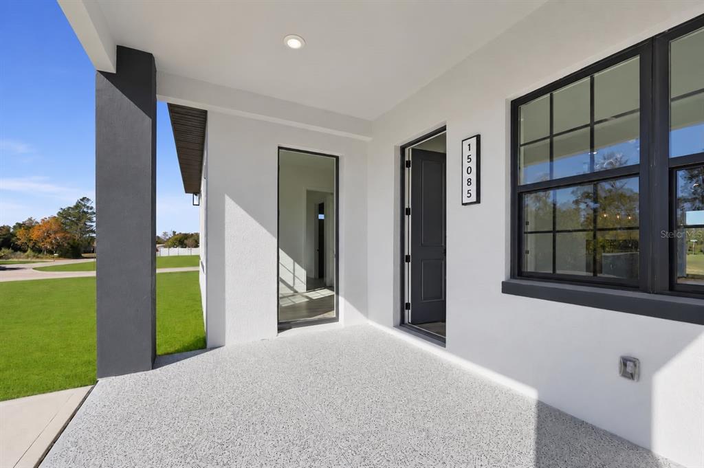 A covered front porch with a gray speckled floor, white walls, and a dark door — 15085 SW 50TH AVENUE ROAD, OCALA, FL