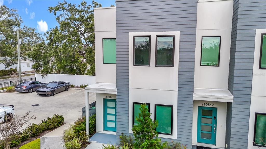 An exterior view of a modern two-story townhouse with teal doors and gray siding — 2108 E 22ND AVENUE UNIT 1, TAMPA, FL