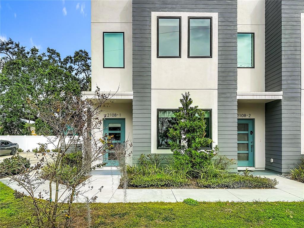 The exterior of a modern two-unit townhouse features gray siding, white stucco, and teal doors — 2108 E 22ND AVENUE UNIT 1, TAMPA, FL