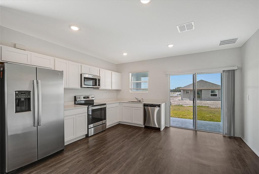 A kitchen with white cabinets, stainless steel appliances, and dark wood-look flooring leads to a patio — 13028 SASSAFRAS TRAIL, PARRISH, FL