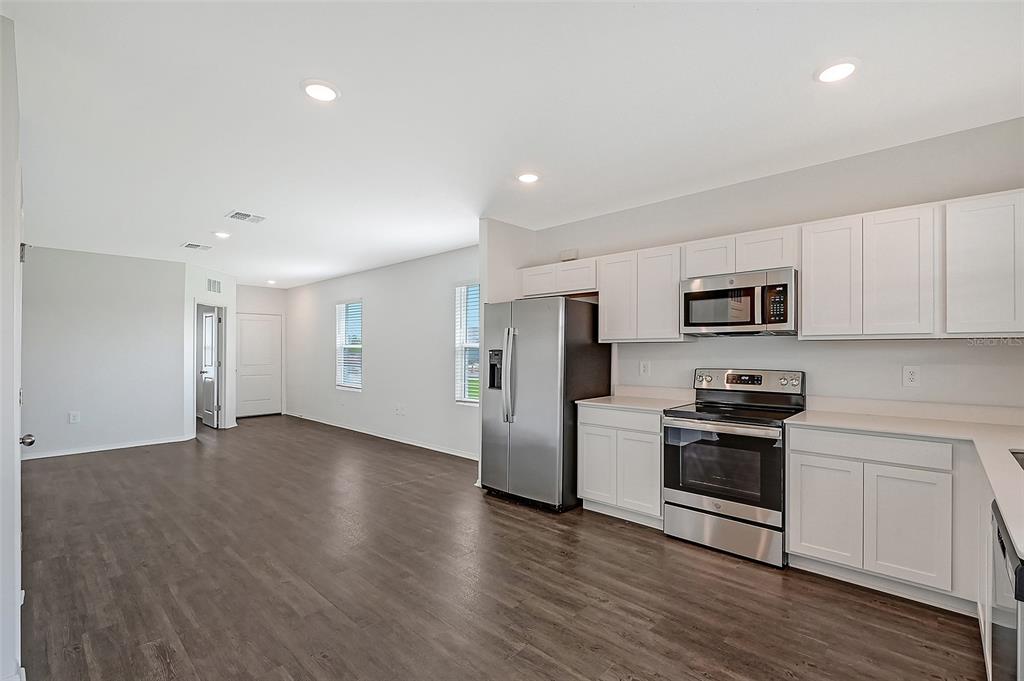A kitchen with white cabinets and stainless steel appliances opens into a spacious living area — 13028 SASSAFRAS TRAIL, PARRISH, FL