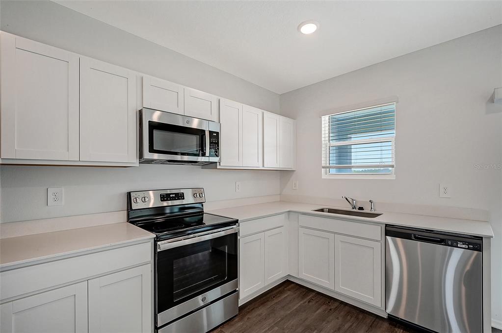 A kitchen features white cabinets, stainless steel appliances, a window, and dark wood-look flooring — 13028 SASSAFRAS TRAIL, PARRISH, FL