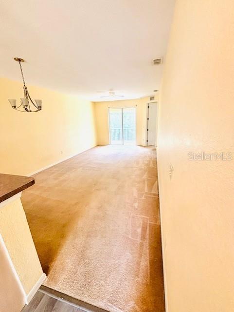 An empty living room features beige carpeting, yellow walls, and a hanging chandelier — 14201 INDIAN CREEK DRIVE UNIT 14201, KISSIMMEE, FL