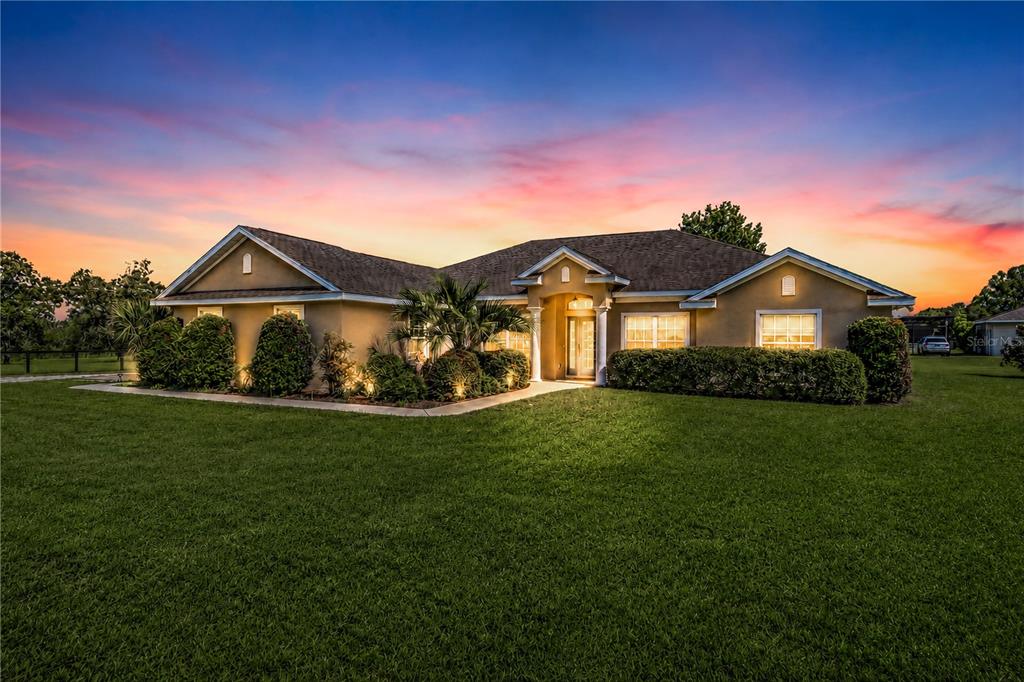 A single-story house with a tan exterior and a large lawn at sunset — 16051 SW 30TH LANE, OCALA, FL