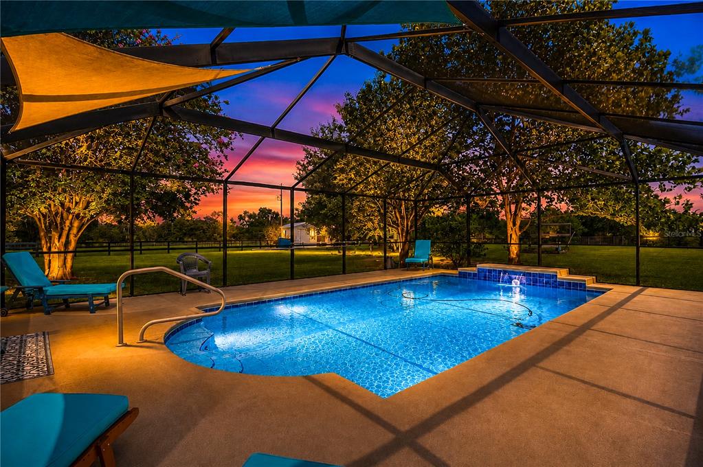A screened-in swimming pool with a water feature at sunset in a grassy backyard — 16051 SW 30TH LANE, OCALA, FL