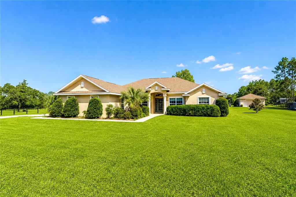 A tan, single-story house with a shingled roof sits on a large, grassy lawn — 16051 SW 30TH LANE, OCALA, FL