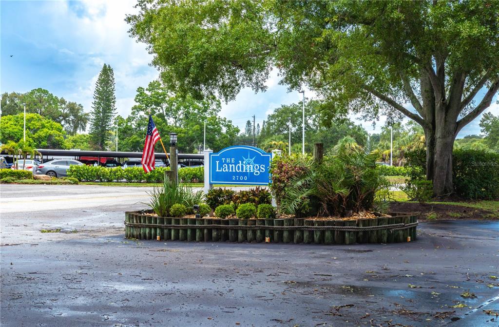 A blue sign for The Landings stands in a landscaped bed with an American flag — 2700 NEBRASKA AVENUE UNIT 2-205, PALM HARBOR, FL