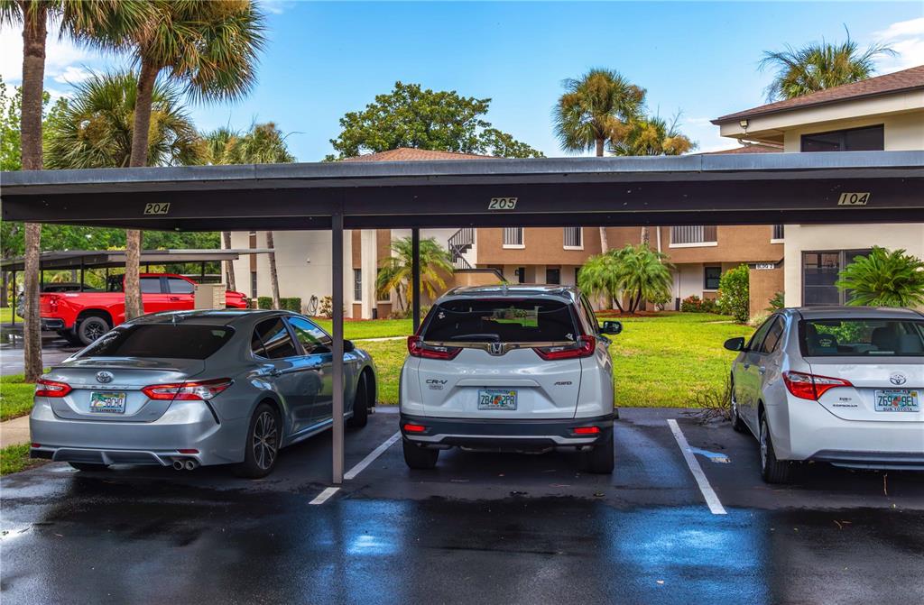 A covered parking area with three parked cars in front of a multi-story apartment building — 2700 NEBRASKA AVENUE UNIT 2-205, PALM HARBOR, FL