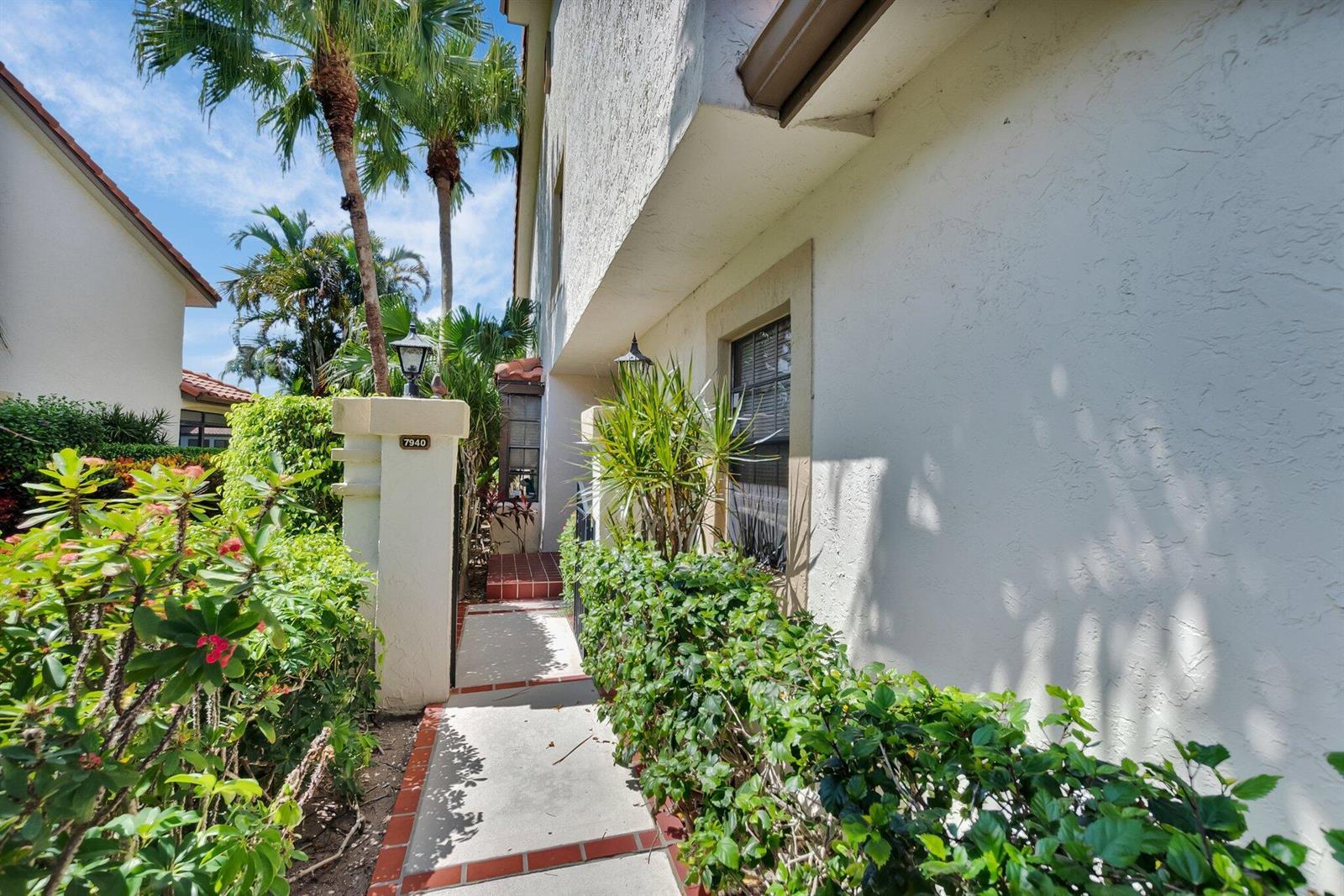 A concrete walkway leads to the entrance of a white stucco building with lush landscaping — 7940 La Mirada Drive, Boca Raton FL 33433, BOCA RATON, FL