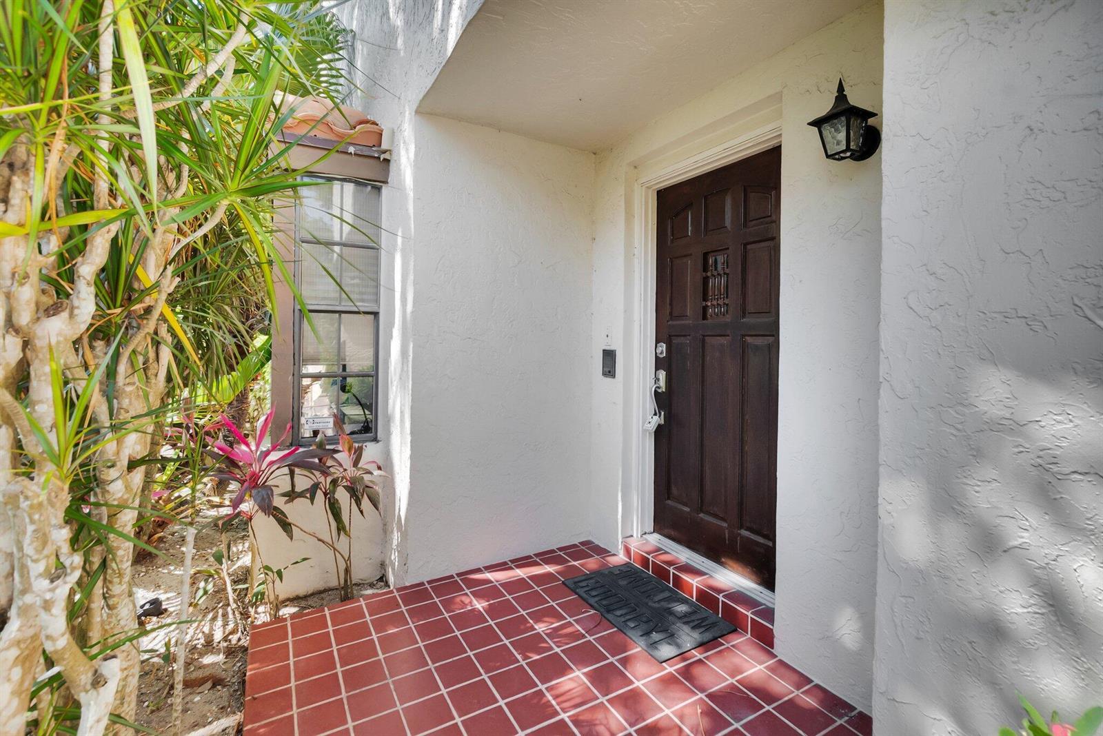 A dark wooden front door opens onto a red tiled porch with a welcome mat — 7940 La Mirada Drive, Boca Raton FL 33433, BOCA RATON, FL