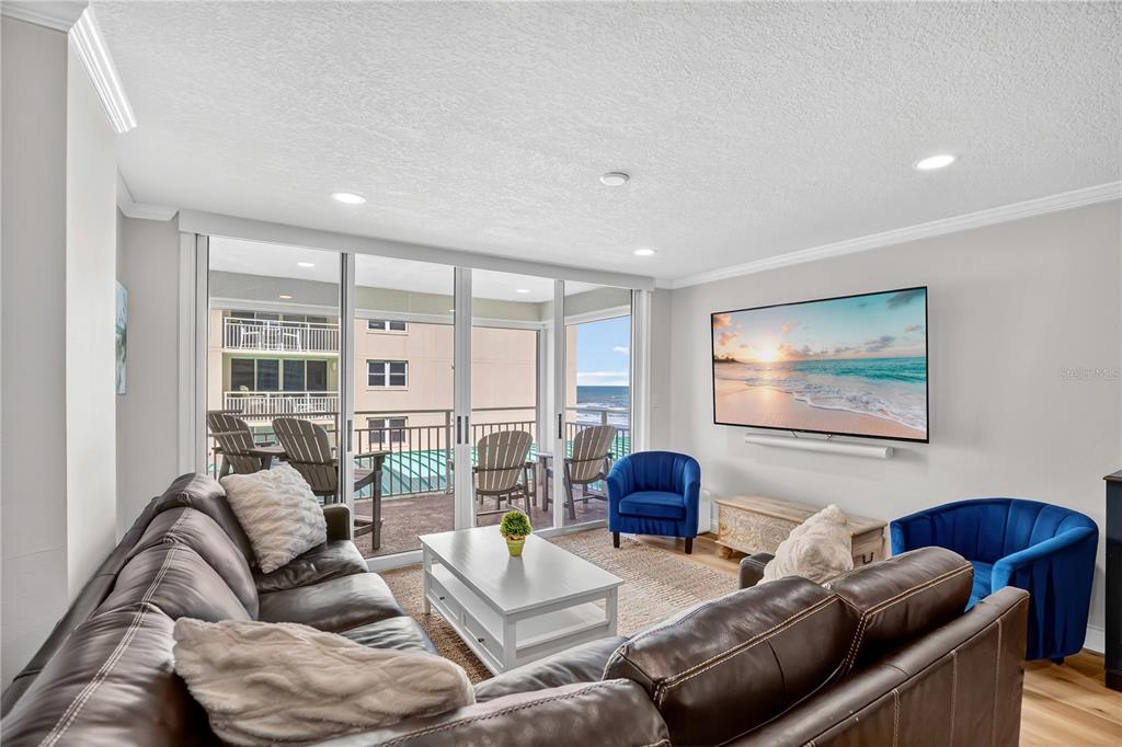A living room features a brown leather sectional, blue armchairs, and a balcony with seating — 4505 S ATLANTIC AVENUE UNIT 305, PONCE INLET, FL