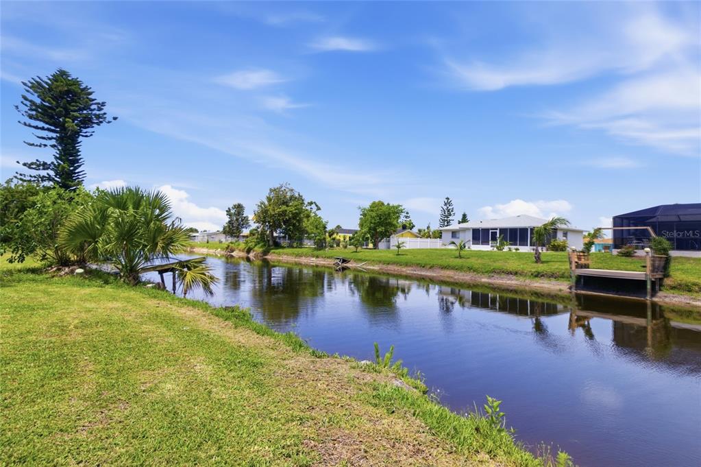 A canal view from a grassy backyard featuring a small wooden dock and nearby houses — 52 ANNAPOLIS LANE, ROTONDA WEST, FL