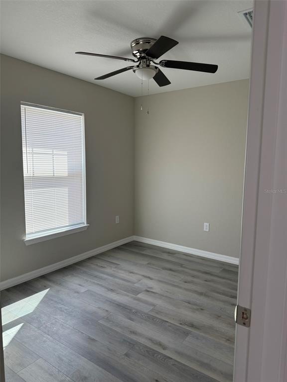An empty room features gray wood-look flooring, light-colored walls, a ceiling fan, and a window — 9539 N TRAVIS DRIVE UNIT B, CITRUS SPRINGS, FL