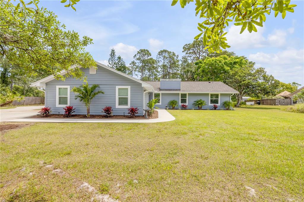 A single-story blue house with white trim sits on a grassy lot with trees — 106 PINE TREE DRIVE, ORMOND BEACH, FL