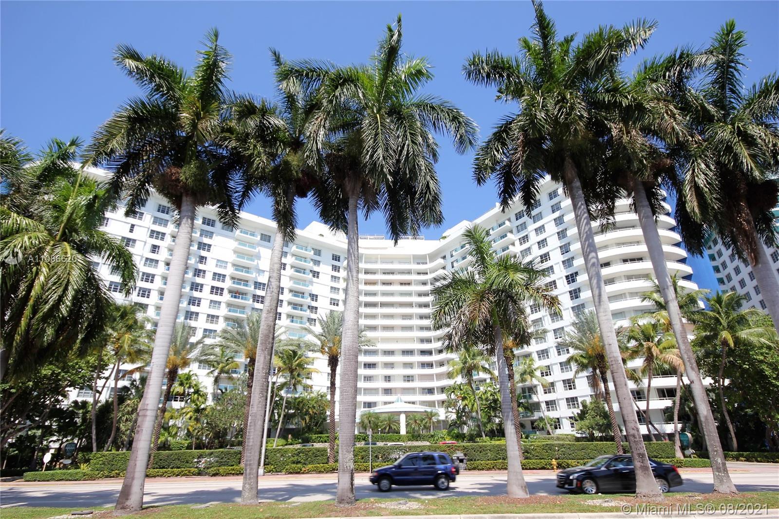 A multi-story white residential building is framed by tall palm trees along a street — 5151 COLLINS AV # 1030, Miami Beach FL 33140, MIAMI BEACH, FL