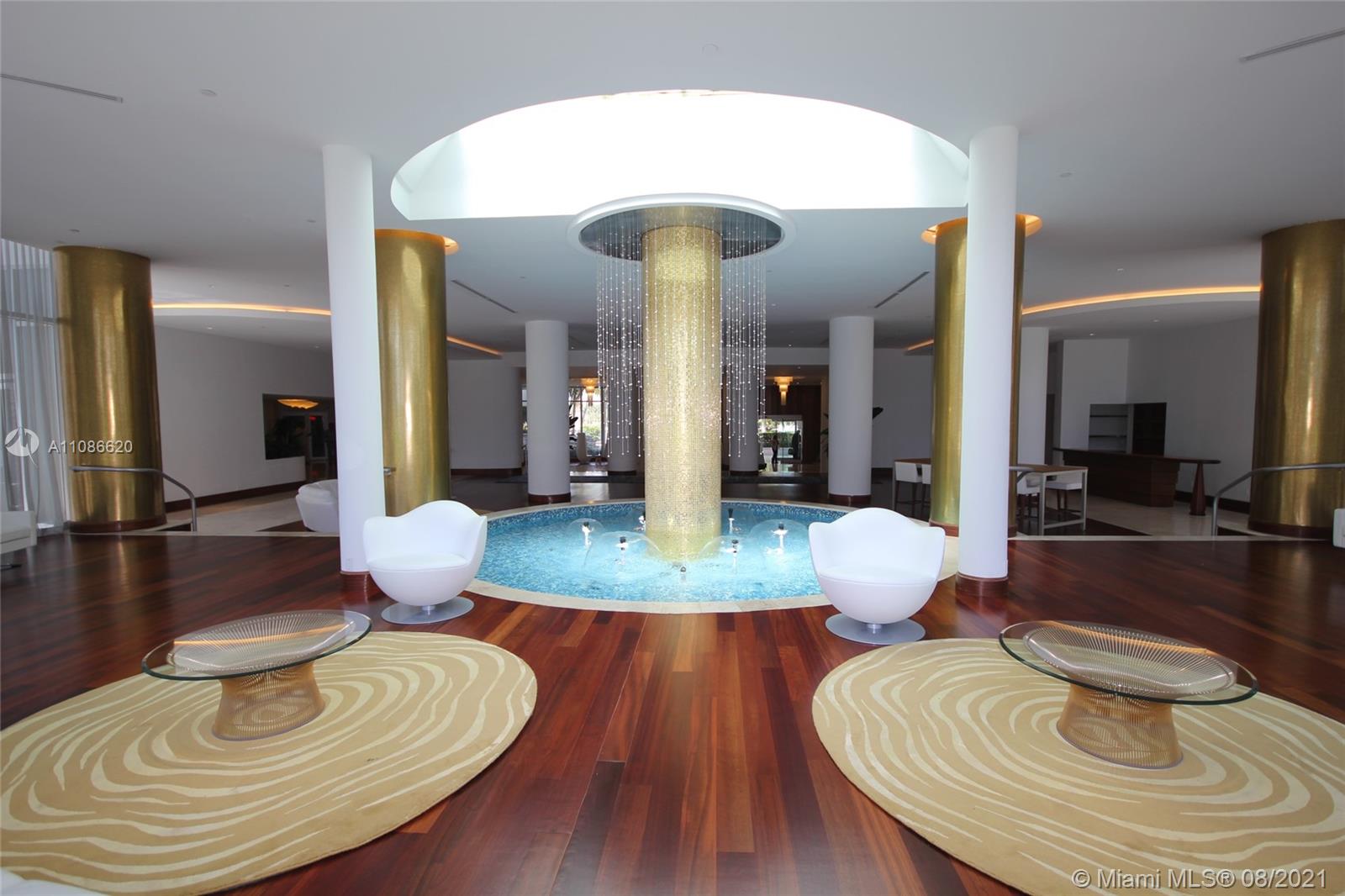 A lobby features a central circular fountain, gold columns, and modern white chairs on wood floors — 5151 COLLINS AV # 1030, Miami Beach FL 33140, MIAMI BEACH, FL