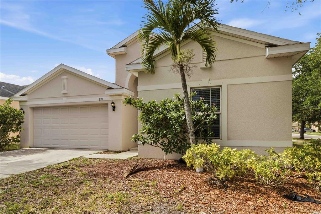 A single-story house with a beige stucco exterior, a two-car garage, and a palm tree — 820 PARKER DEN DRIVE, RUSKIN, FL
