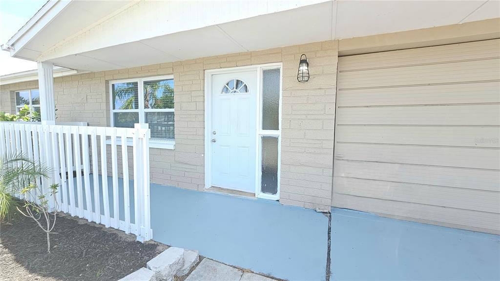 A tan brick house exterior features a white front door, a garage, and a white fence — 6412 PAWLING AVENUE, PORT RICHEY, FL