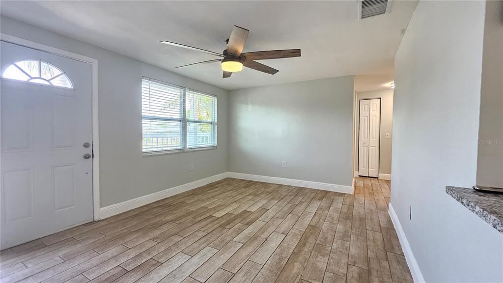 A room with light gray walls, wood-look tile flooring, a ceiling fan, and a front door — 6412 PAWLING AVENUE, PORT RICHEY, FL