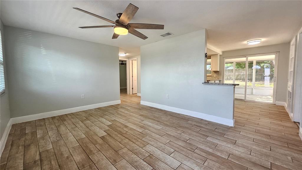 A living room with wood-look tile flooring, a ceiling fan, and a view into the kitchen — 6412 PAWLING AVENUE, PORT RICHEY, FL