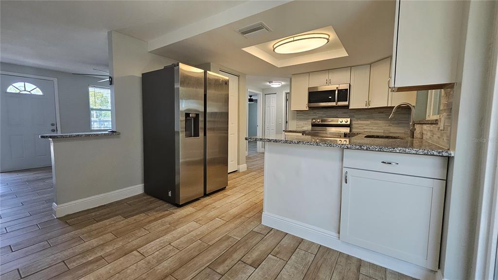 A kitchen with stainless steel appliances, white cabinets, and granite countertops over wood-look tile flooring — 6412 PAWLING AVENUE, PORT RICHEY, FL
