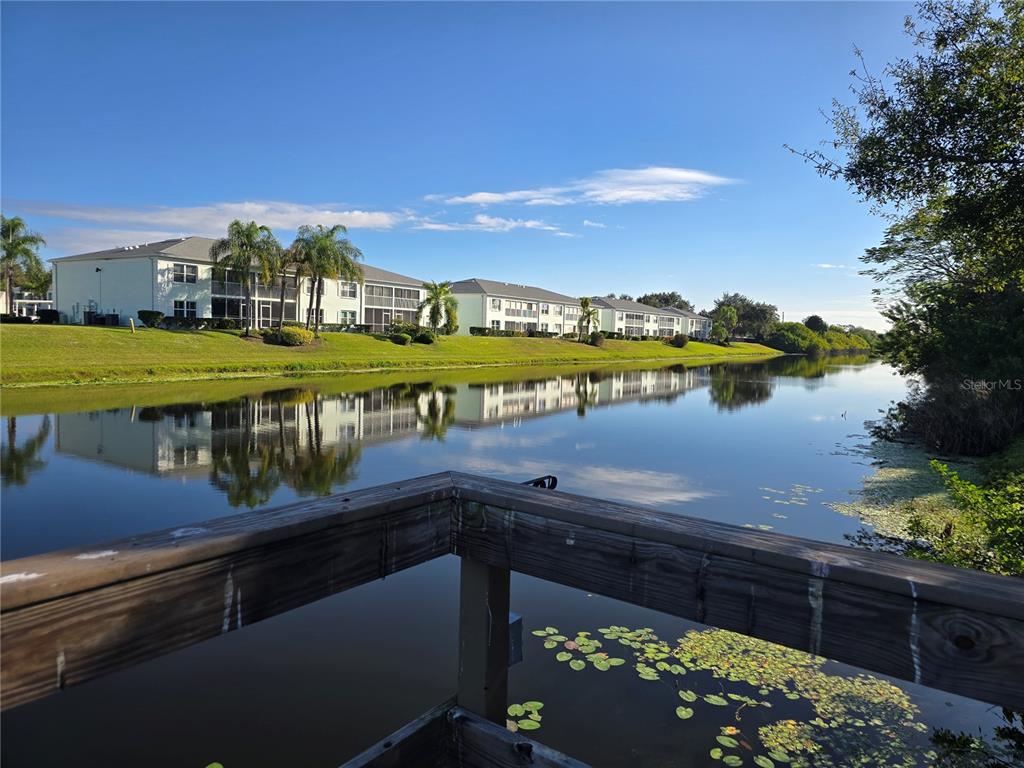 A wooden deck overlooks a calm pond with apartment buildings in the background — 5722 ESPANOLA AVENUE, NORTH PORT, FL