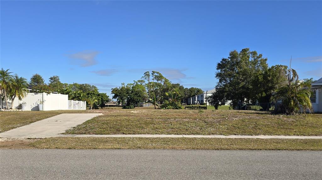 A vacant, grassy residential lot features a concrete driveway apron and surrounding trees — 5722 ESPANOLA AVENUE, NORTH PORT, FL