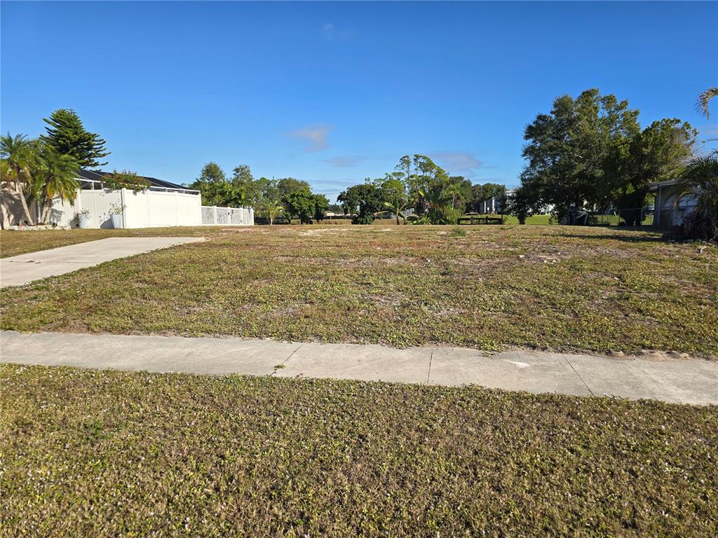 A vacant, grassy residential lot features a concrete driveway and sidewalk under a clear sky — 5722 ESPANOLA AVENUE, NORTH PORT, FL