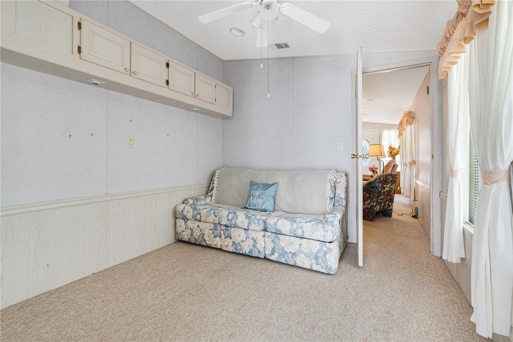 A room with beige carpet, floral sofa, wall-mounted cabinets, and a doorway leading to another room — 9000 US HIGHWAY 192 UNIT 517, CLERMONT, FL