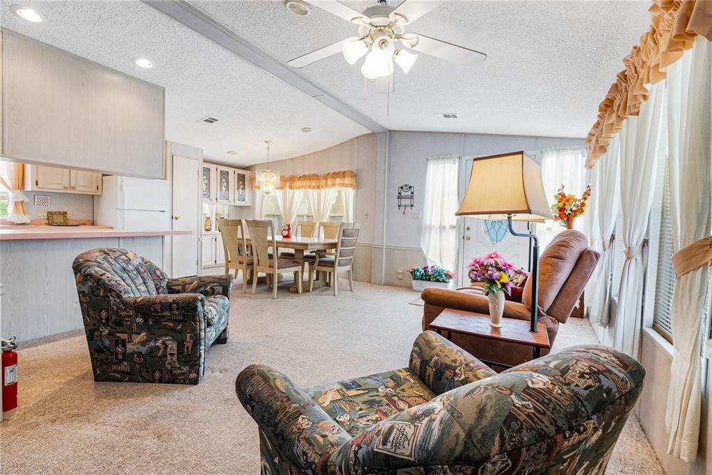 A living room and dining area featuring patterned armchairs, a recliner, and light-colored carpeting — 9000 US HIGHWAY 192 UNIT 517, CLERMONT, FL